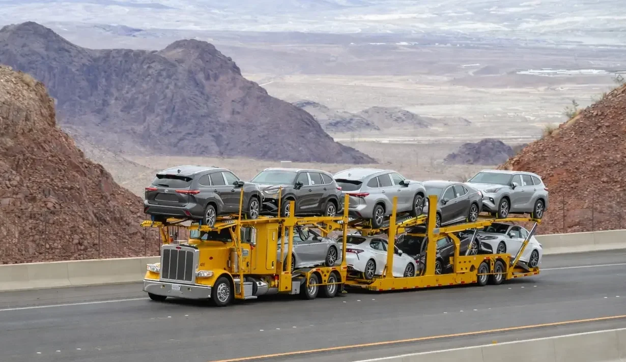 Yellow car carrier transporting dealership inventory through a mountain highway.