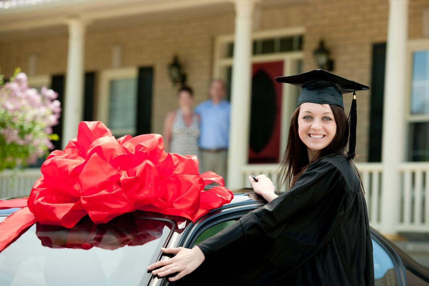 College graduate standing beside a new car with a red bow